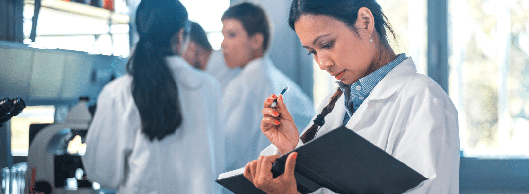 females in lab coats one in foreground about to write results